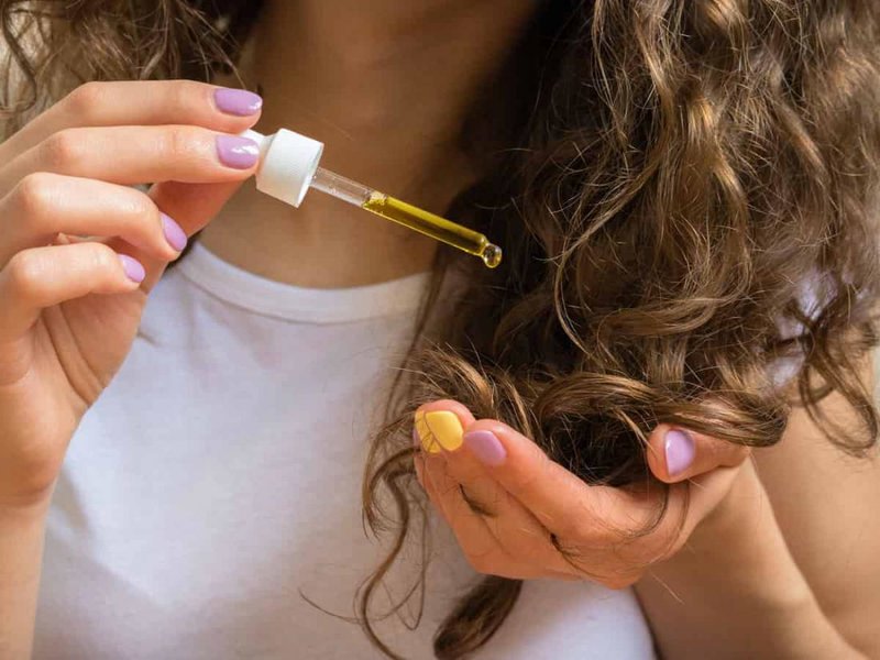 Fille utilise de l'huile de jojoba au bout de ses cheveux