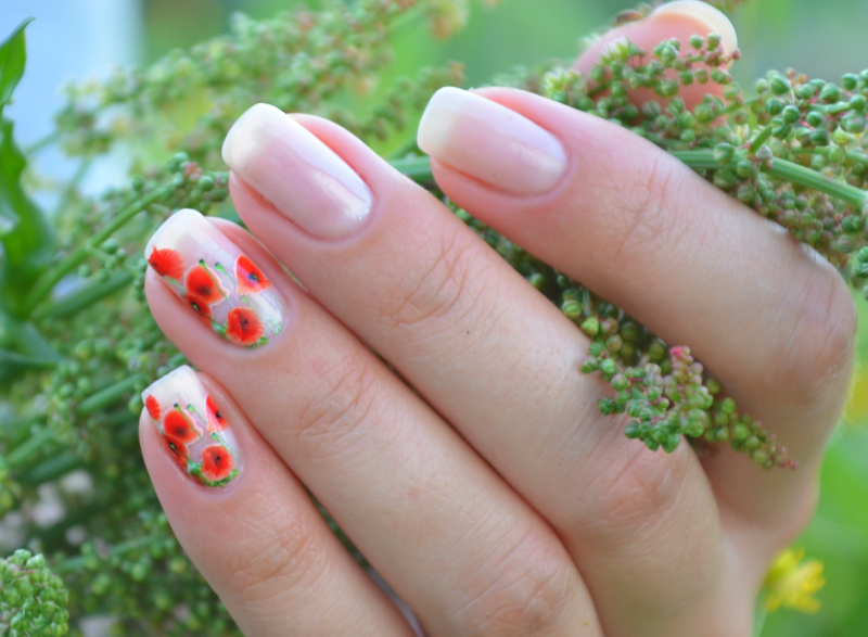 Manucure nue avec des autocollants en forme de coquelicots.